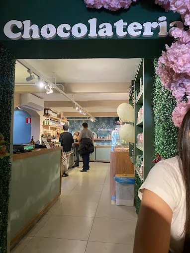 Entrada interna sob o letreiro Chocolateria, entre paredes de folhagem
